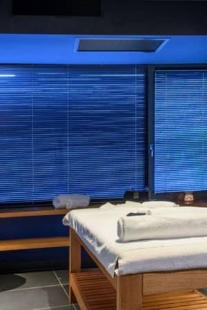 Lyttos Mare spa room with massage table, wooden bench, candles, and deep blue walls for a calming atmosphere.