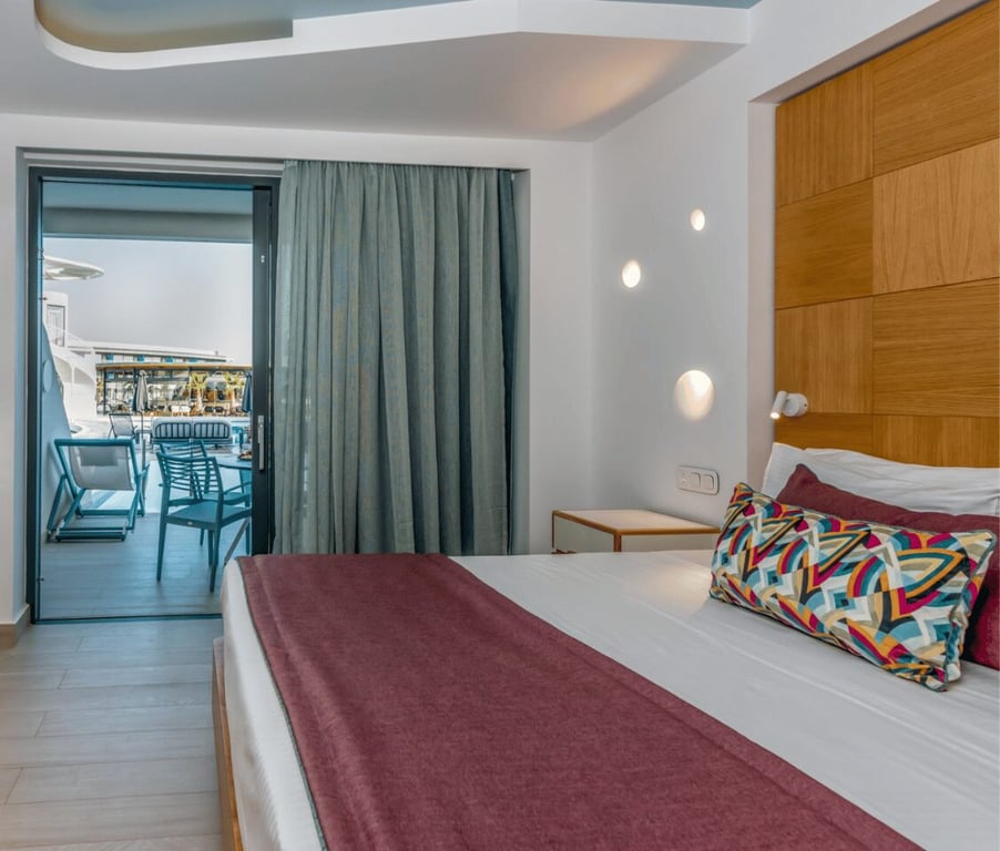 Luxury hotel room at Lyttos Mare with king-sized bed and private balcony overlooking the sea, featuring modern decor and ambient lighting.