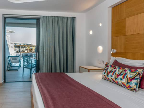 Luxury hotel room at Lyttos Mare with king-sized bed and private balcony overlooking the sea, featuring modern decor and ambient lighting.
