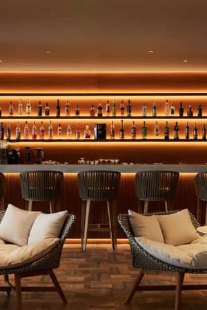 Sophisticated bar in Marbella Gallery, with wooden bar counter, high stools, and ambient lighting, featuring an array of spirits on shelves.