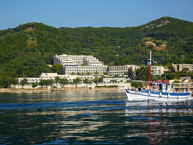 Traditional boat on calm water with a hillside resort and lush greenery in the background at Marbella.