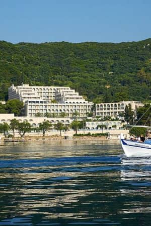 Traditional boat on calm water with a hillside resort and lush greenery in the background at Marbella.