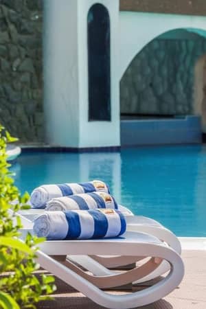 Poolside loungers with blue and white striped towels beside a clear swimming pool at a Marbella resort.