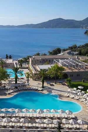 Aerial view of Marbella Gallery resort with two heart-shaped swimming pools, surrounded by sun loungers and palm trees, overlooking the sea and mountains.