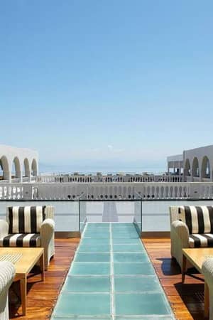 Veranda at Marbella Gallery with elegant striped furniture and palm trees, overlooking a sea view with grand arches.