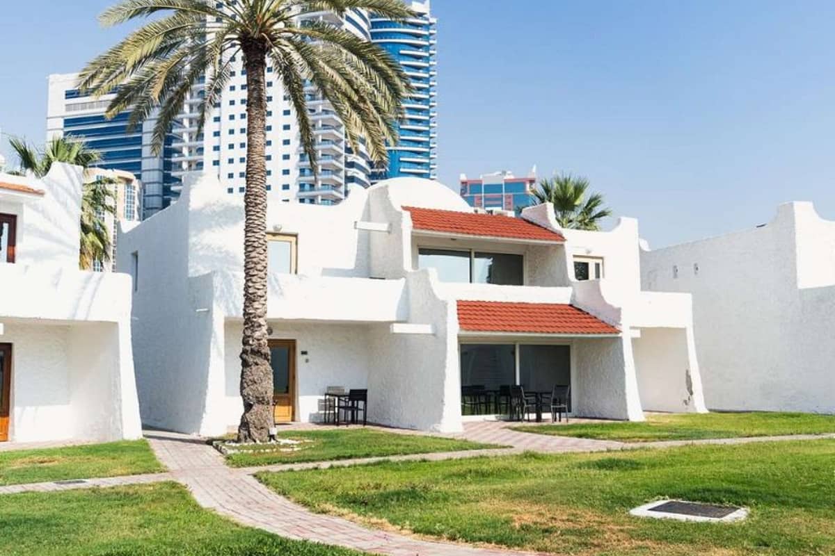 White-washed villas at Marbella Gallery with green lawns, a palm tree, and skyscrapers in the background.