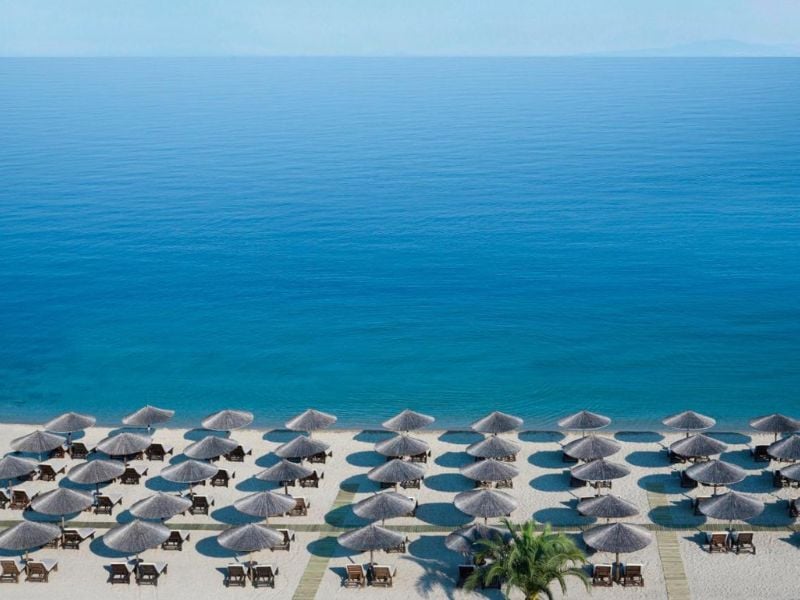 Aerial view of a beach with straw parasols and wooden lounge chairs by the calm sea at Meliton Gallery.