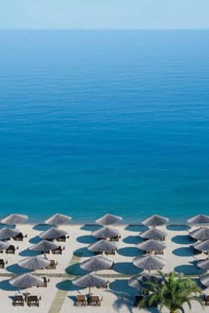 Aerial view of a beach with straw parasols and wooden lounge chairs by the calm sea at Meliton Gallery.