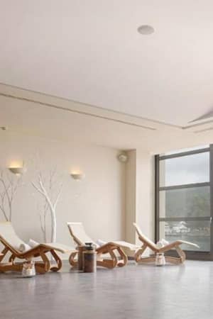 Indoor lounge of Meliton Gallery with wooden reclining chairs and a large window showing a lake and greenery.
