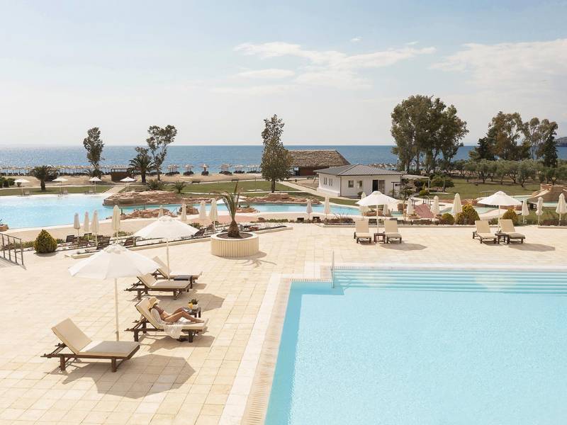 Meliton Gallery poolside with two swimming pools, sun loungers, umbrellas, and a view of the beach and sea.