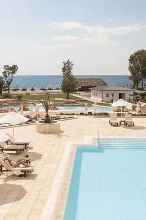 Meliton Gallery poolside with two swimming pools, sun loungers, umbrellas, and a view of the beach and sea.