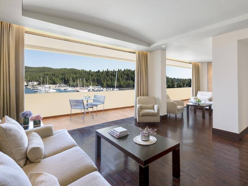 Modern hotel room in Meliton Gallery with a balcony overlooking a marina and forest, furnished with sofas and armchairs.