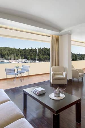 Modern hotel room in Meliton Gallery with a balcony overlooking a marina and forest, furnished with sofas and armchairs.