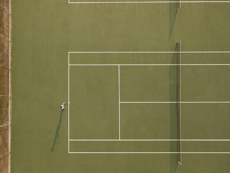 Aerial view of a tennis court at Meliton Gallery with a single tennis player preparing to serve.