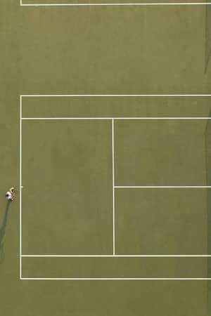 Aerial view of a tennis court at Meliton Gallery with a single tennis player preparing to serve.