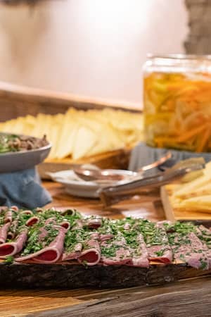 Spread of cheeses and cured meats at Mira Alagna Mountain Resort & Spa with marinated vegetables, arranged on wooden platters.
