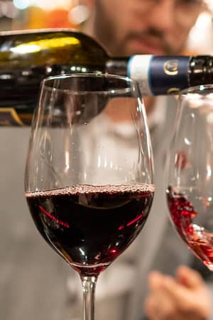 Bartender pouring red wine into glasses in a cosy bar at Mira Alagna Mountain Resort & Spa, with Anfora Grappa bottle visible.