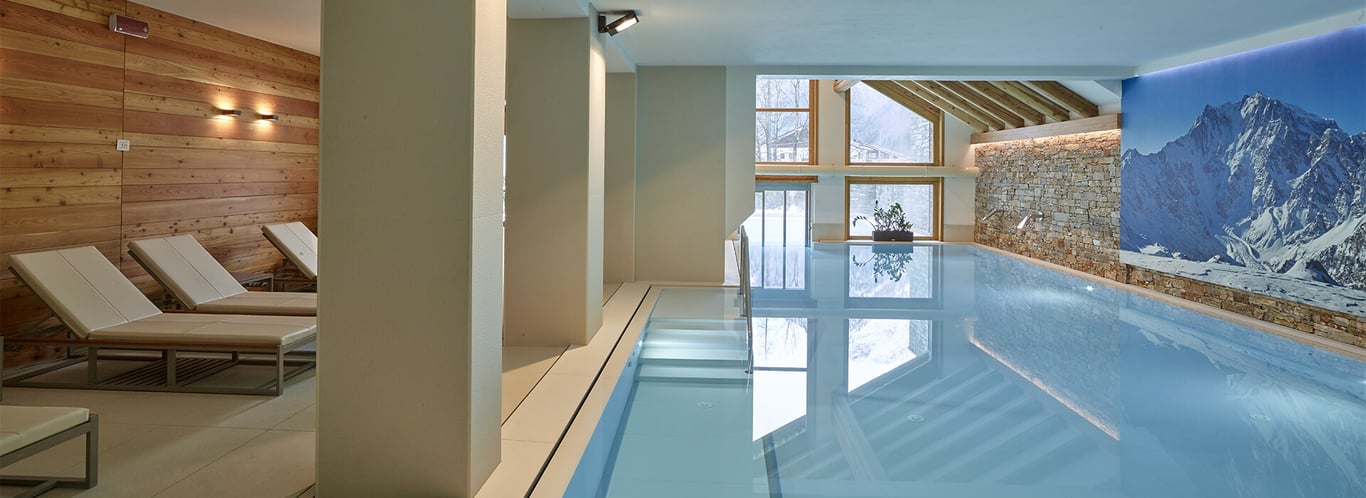Indoor pool at Mira Alagna Mountain Resort & Spa with wooden accents and mountain view through large windows.