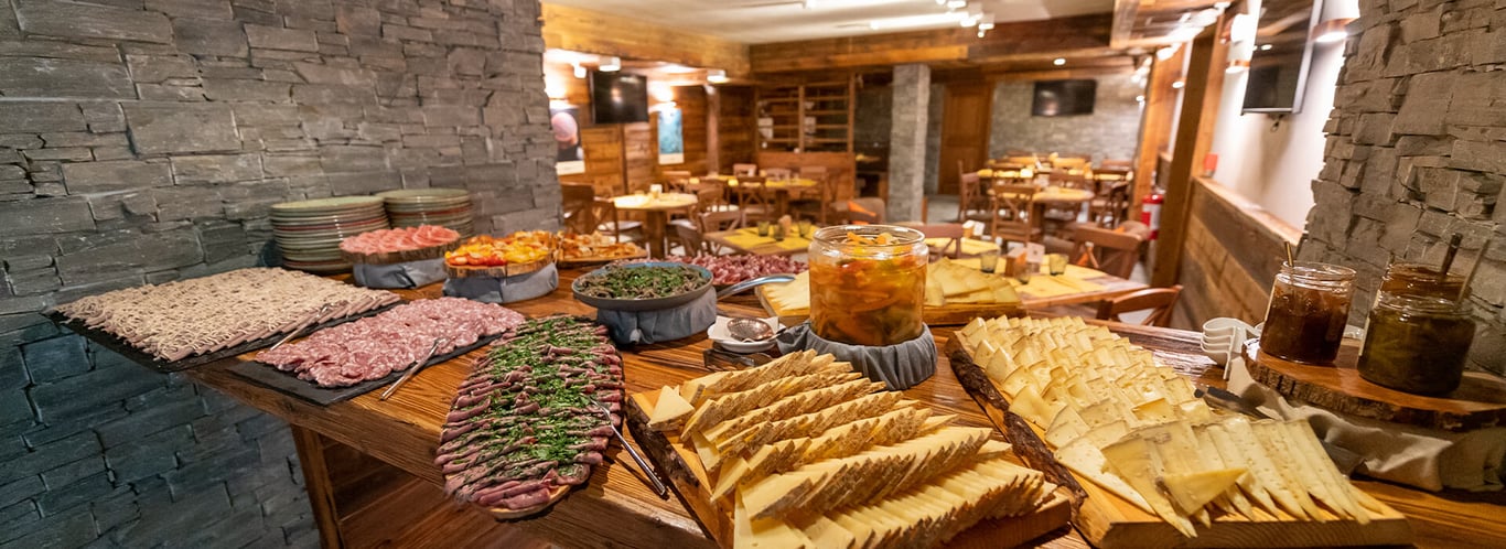 Restaurant at Mira Alagna Mountain Resort & Spa with a spread of meats, cheeses, and preserves, set in a rustic dining room with stone walls.