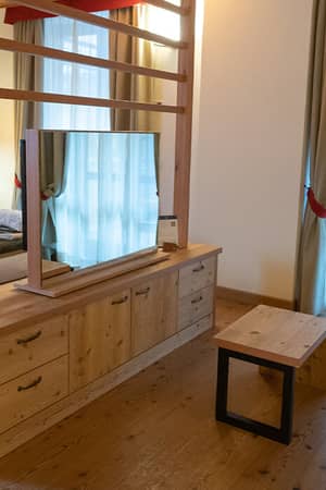 Room interior at Mira Alagna Mountain Resort & Spa featuring a double bed, wooden partition, TV, plaid sofa, and large windows.