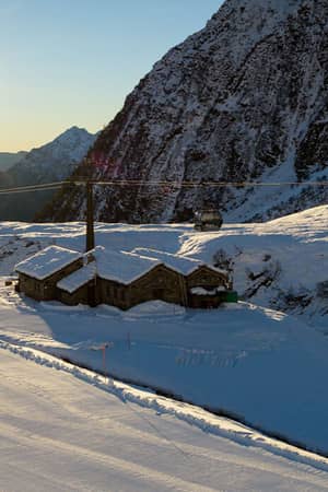 Skiers on snow-covered Mira Alagna Mountain Resort slopes with mountains and a sunset in the background.