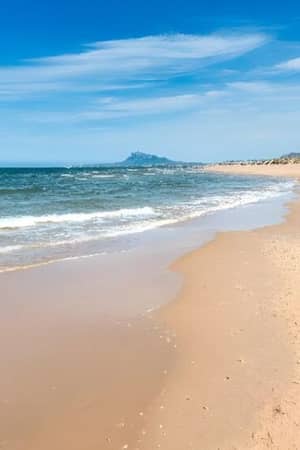 Golden sandy beach at Oliva Nova with gentle waves under a clear blue sky.
