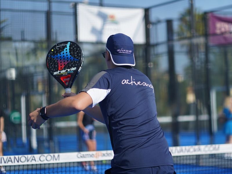 Padel coach in navy activewear branded 'active nova' on a court at Oliva Nova, holding a Startvie paddle mid-swing.