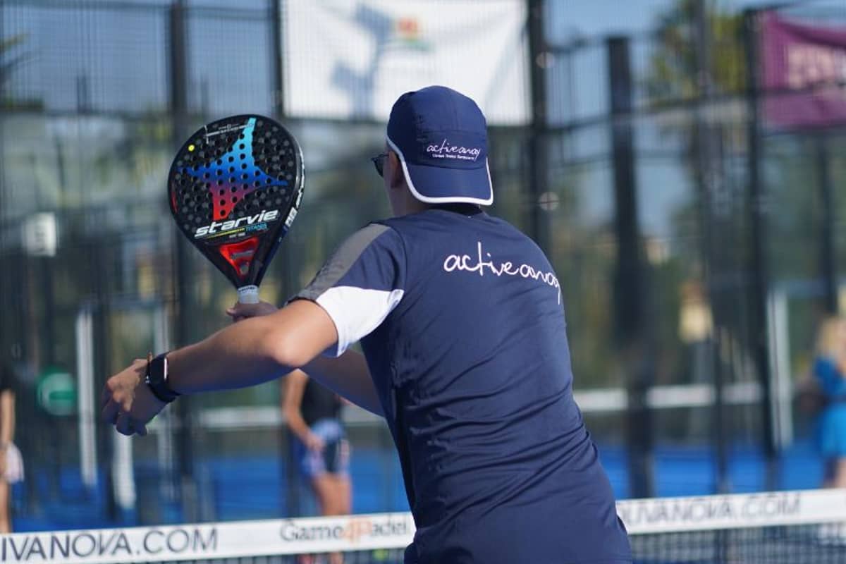 Padel coach in navy activewear branded 'active nova' on a court at Oliva Nova, holding a Startvie paddle mid-swing.
