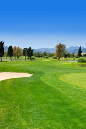 Golf course at Oliva Nova, featuring a sand bunker, fairways, a water hazard, and mountains in the backdrop.