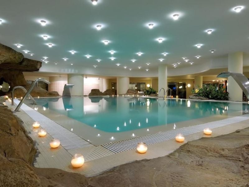 Indoor swimming pool at Oliva Nova Padel with rock formations and candle lighting for a relaxing atmosphere.
