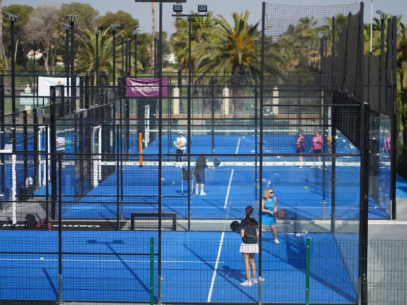 Players on a blue padel court at Oliva Nova Beach & Golf Resort, surrounded by palm trees and netted walls.
