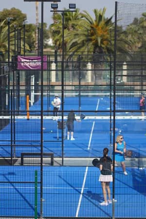 Players on a blue padel court at Oliva Nova Beach & Golf Resort, surrounded by palm trees and netted walls.