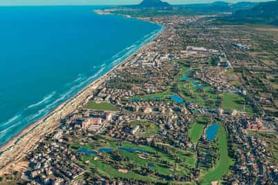 Aerial view of Oliva Nova highlighting golf courses, residential areas, and the Mediterranean coastline with mountains in the background.