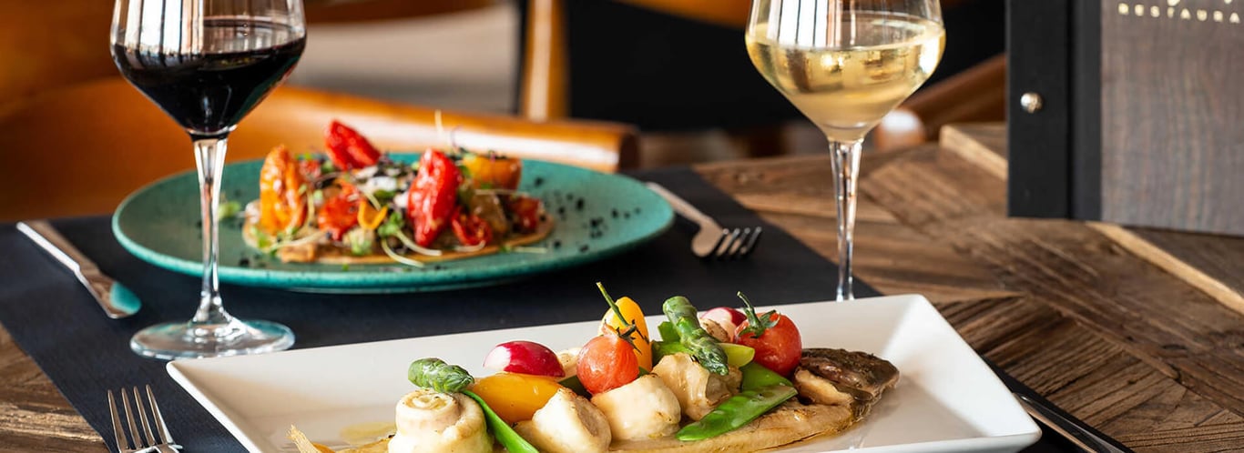 Gourmet dish with scallops and vegetables, served with glasses of red and white wine at Oliva Nova.