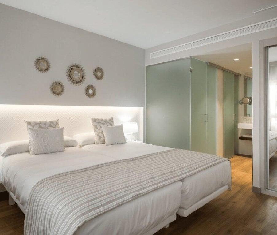 Oliva Nova Premium Room with a double bed, decorative pillows, mirrored wall art, and a modern bathroom with frosted glass doors.