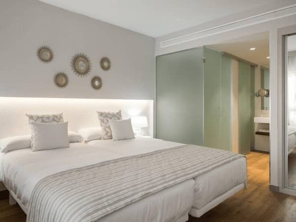 Oliva Nova Premium Room with a double bed, decorative pillows, mirrored wall art, and a modern bathroom with frosted glass doors.
