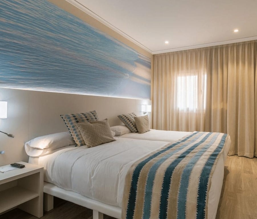 Oliva Nova suite room with decor in blue tones, large bed with throw pillows, and a wall picture of ocean waves.