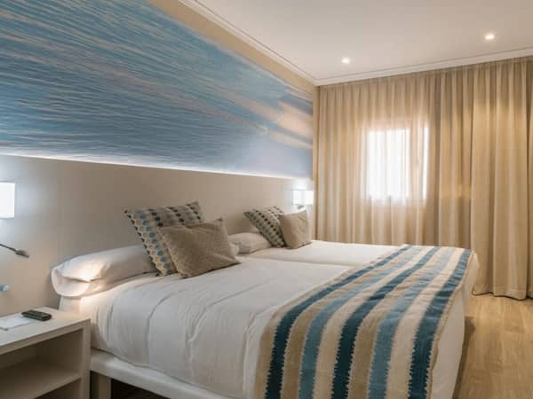 Oliva Nova suite room with decor in blue tones, large bed with throw pillows, and a wall picture of ocean waves.
