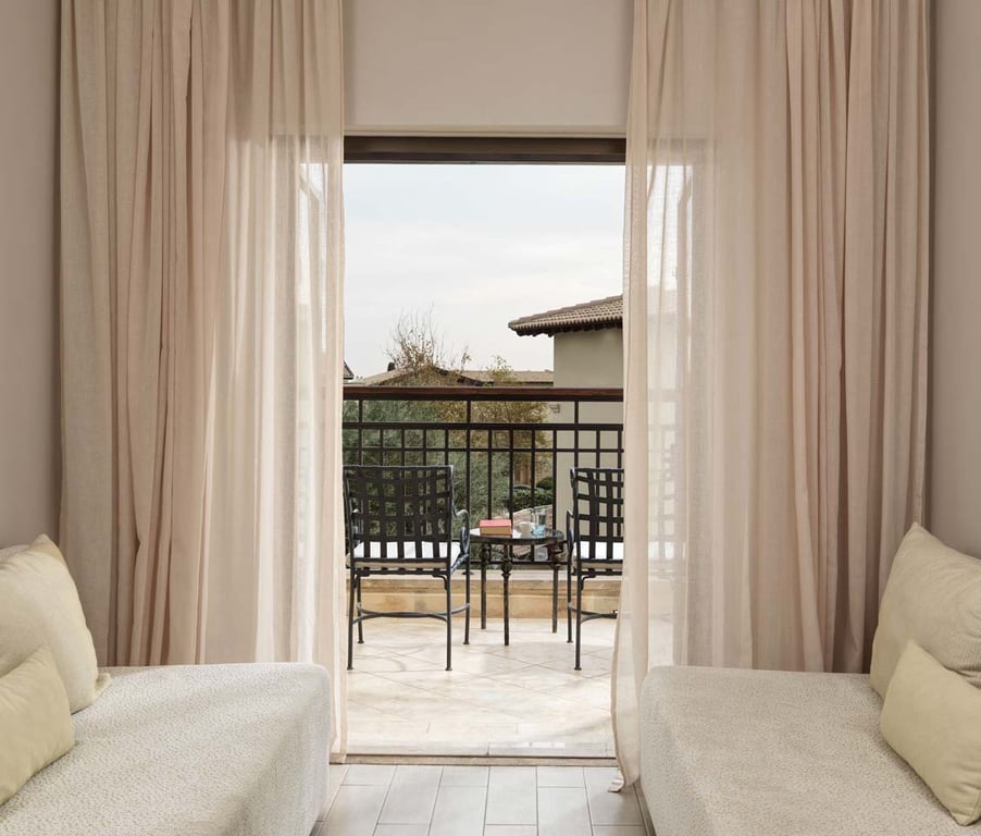 Interior view of a one-bedroom suite with cosy lounge chairs overlooking a balcony with golf and sea views.