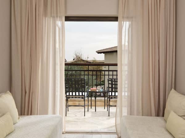 Interior view of a one-bedroom suite with cosy lounge chairs overlooking a balcony with golf and sea views.