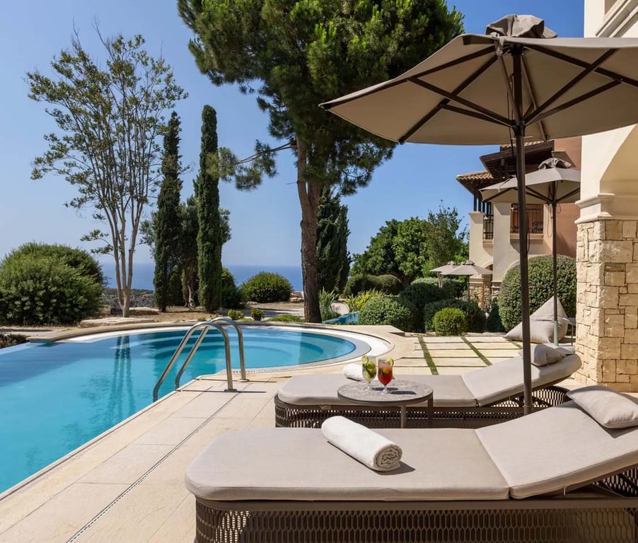 One-bedroom swim-up suite terrace with poolside loungers, overlooking the sea and golf course amidst lush gardens.