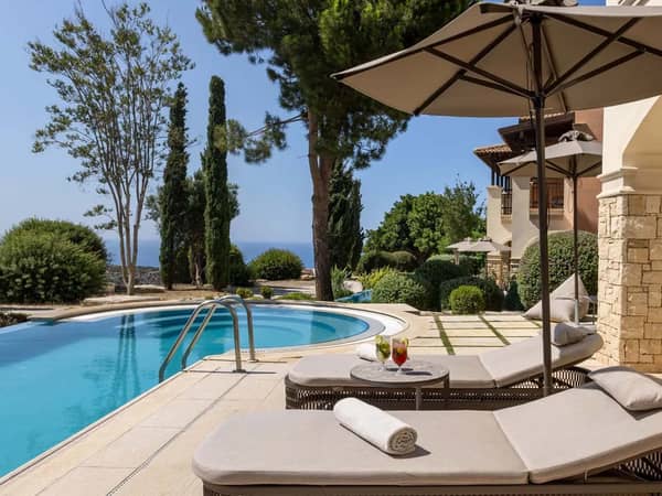 One-bedroom swim-up suite terrace with poolside loungers, overlooking the sea and golf course amidst lush gardens.