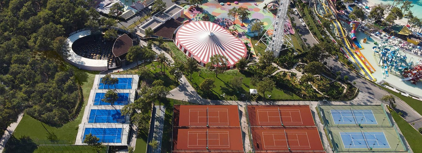 Aerial view of Vogue Hotel Supreme Bodrum featuring tennis courts, a circus-themed area, water slides, and greenery.