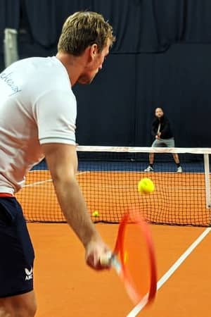 Tennis coaching session at PW Nottingham, featuring a coach preparing to hit a tennis ball with a red racket on indoor courts.