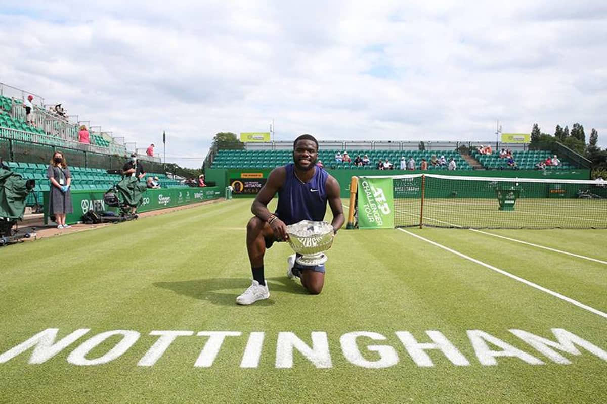 Tennis player smiling and kneeling on the Nottingham grass court while holding a trophy, with 'NOTTINGHAM' written on the court.