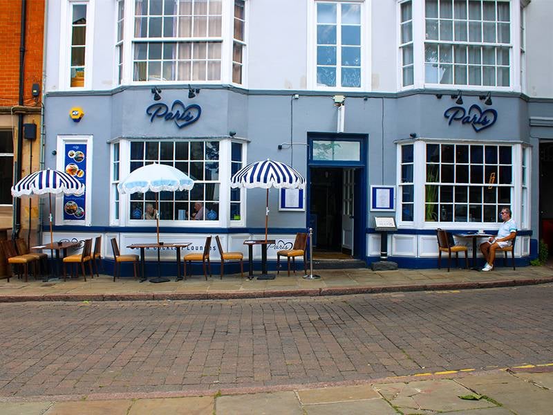 Exterior of Paris restaurant in Nottingham, with outdoor seating under blue and white striped umbrellas on a cobblestone street.