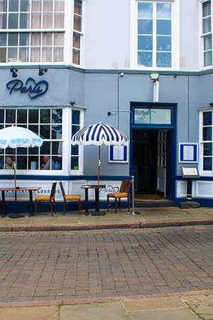 Exterior of Paris restaurant in Nottingham, with outdoor seating under blue and white striped umbrellas on a cobblestone street.