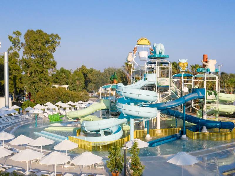 Kids' pool with multiple colourful water slides, sun loungers, parasols, and cartoon animal figures at Paloma Family Holidays.
