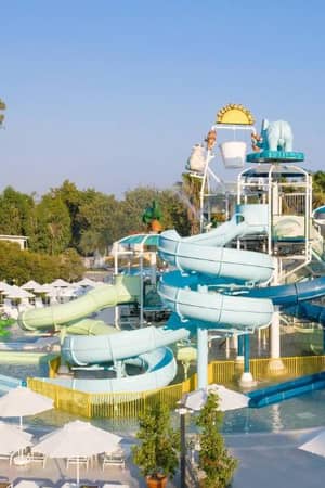 Kids' pool with multiple colourful water slides, sun loungers, parasols, and cartoon animal figures at Paloma Family Holidays.