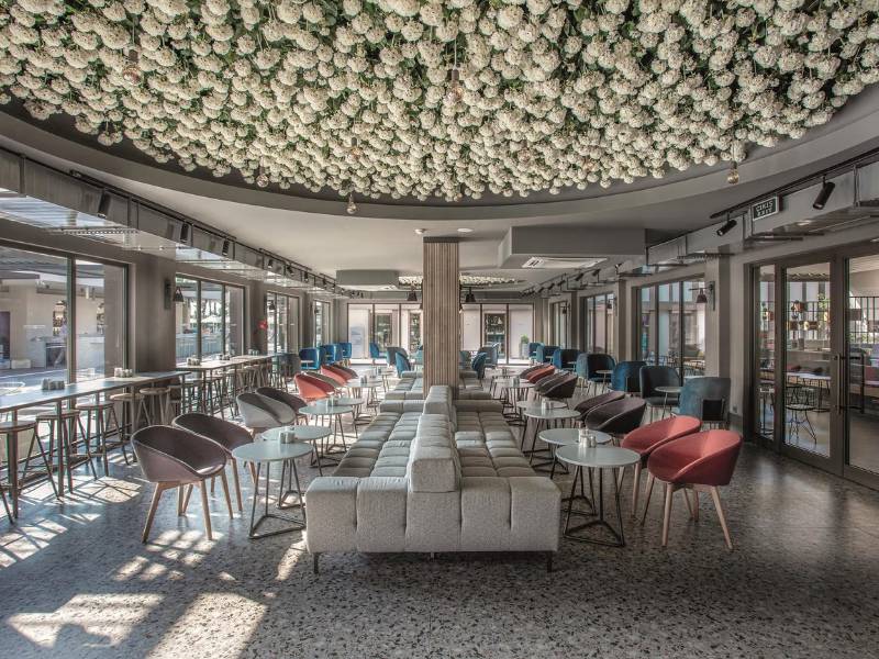 Lounge area at Paloma Family Holidays with white floral ceiling, grey sofas, red chairs, and ample natural light.